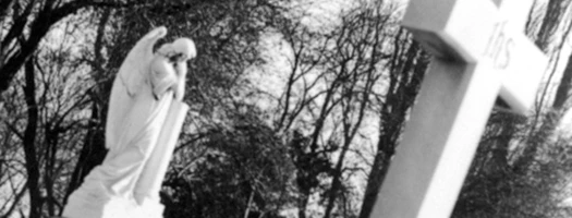 Black and white photo of a cross, stark trees in background creating eerie, haunting atmosphere